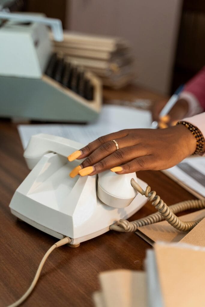 Close-up of a hand with manicured nails using a retro rotary phone in a vintage office setting.